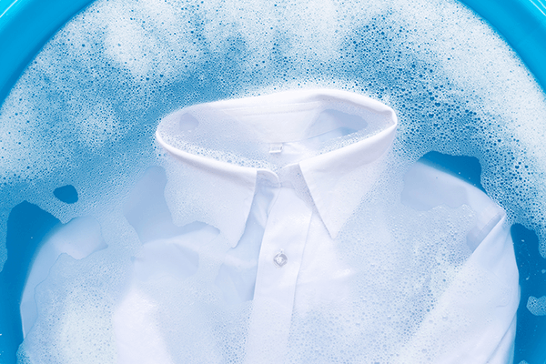 Dress shirt soaking in a blue bowl filled with foamy soapy water, ready for gentle cleaning.