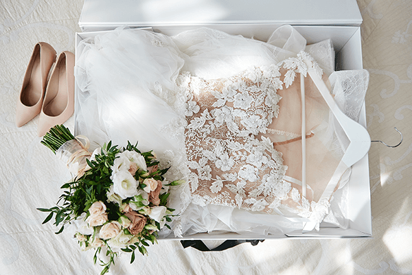 Wedding gown carefully preserved in a keepsake box, accompanied by bridal shoes and a bouquet of flowers.